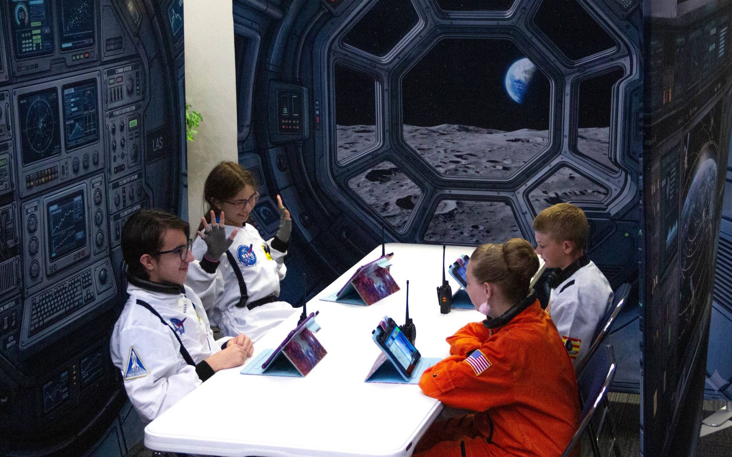 students in front of space station themed backgrounds, while sitting at a table working together