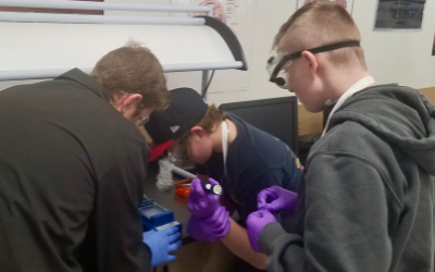 Three students crowd around lab equipment.
